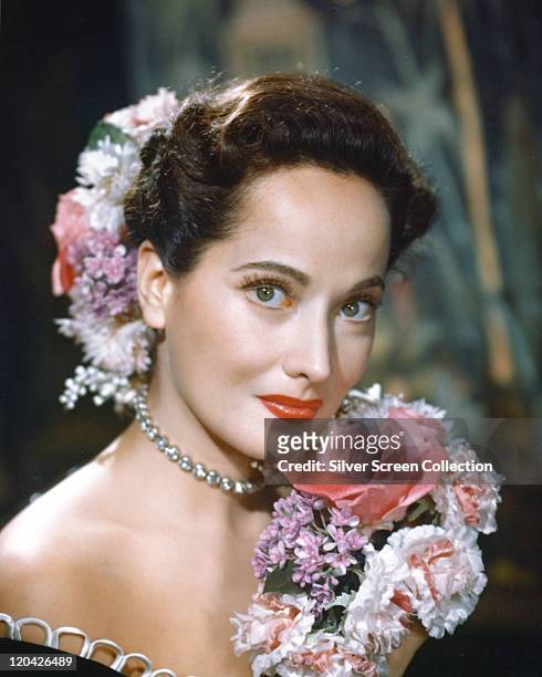 Merle Oberon , British actress, poses with a bouquet of flowers, with flowers in her hair, in a studio portrait, circa 1940.
