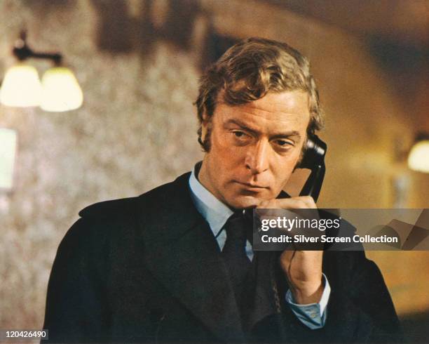 Michael Caine, British actor, wearing a black raincoat and holding a black telephone receiver in a publicity still issued for the film, 'Get Carter',...