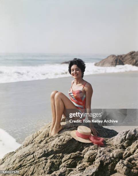 young woman sitting on rock beside sea, smiling, portrait - archival beach stock pictures, royalty-free photos & images