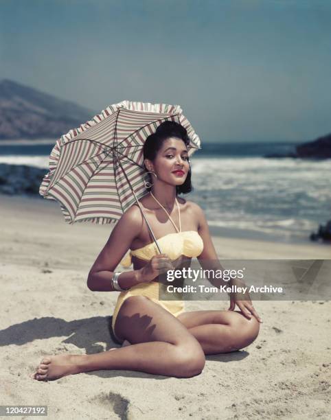 woman in bikini sitting on beach holding umbrella, smiling, portrait - vintage 1950s woman stock pictures, royalty-free photos & images