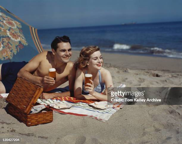 young couple lying on beach with beer, smiling - 1950s man stockfoto's en -beelden