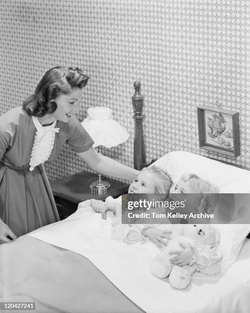 mother tucking daughters into bed, smiling - 1950s bedroom stock pictures, royalty-free photos & images