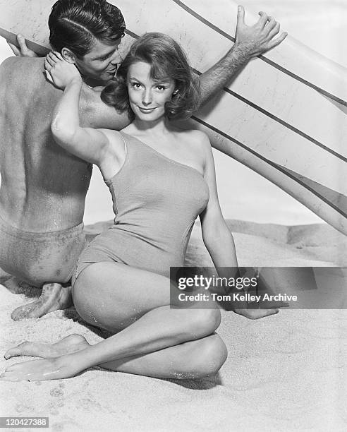 pareja joven con tabla de surf en la playa, sonriendo - 1962 fotografías e imágenes de stock