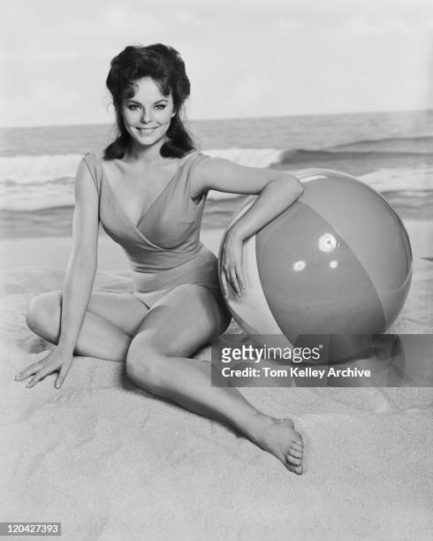 young woman sitting on beach with ball, smiling, portrait - archival 1960s stock pictures, royalty-free photos & images