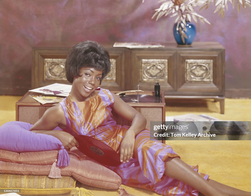 Young woman leaning on cushions holding record, smiling, portrait