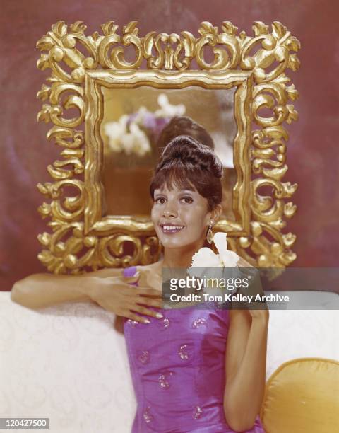mujer joven sentada en el sofá de retención de flor, sonriendo, vertical - 1965 fotografías e imágenes de stock