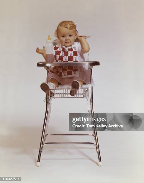 baby girl in high chair holding plate, portrait - baby bib stock pictures, royalty-free photos & images