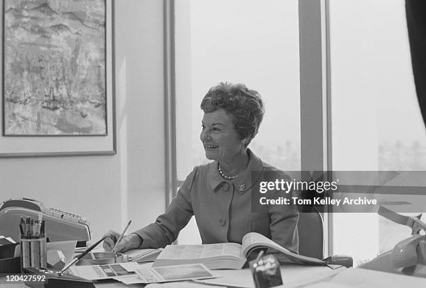 senior mujer sentada en escritorio, sonriente escribiendo en el cuaderno de notas - años 60 fotografías e imágenes de stock