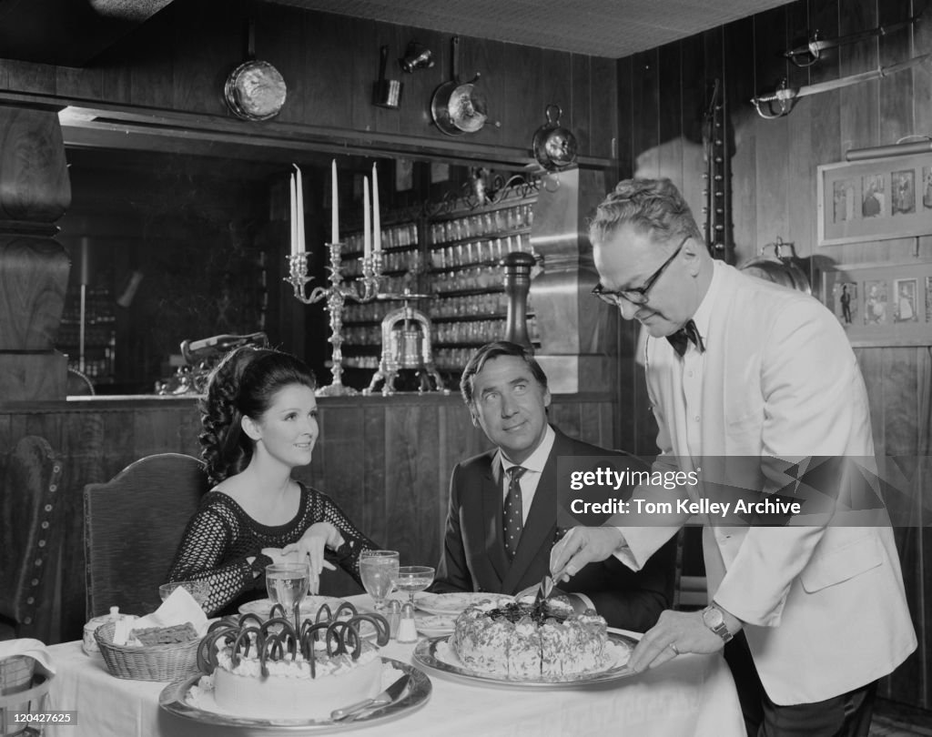 Waiter serving cake to couple at table