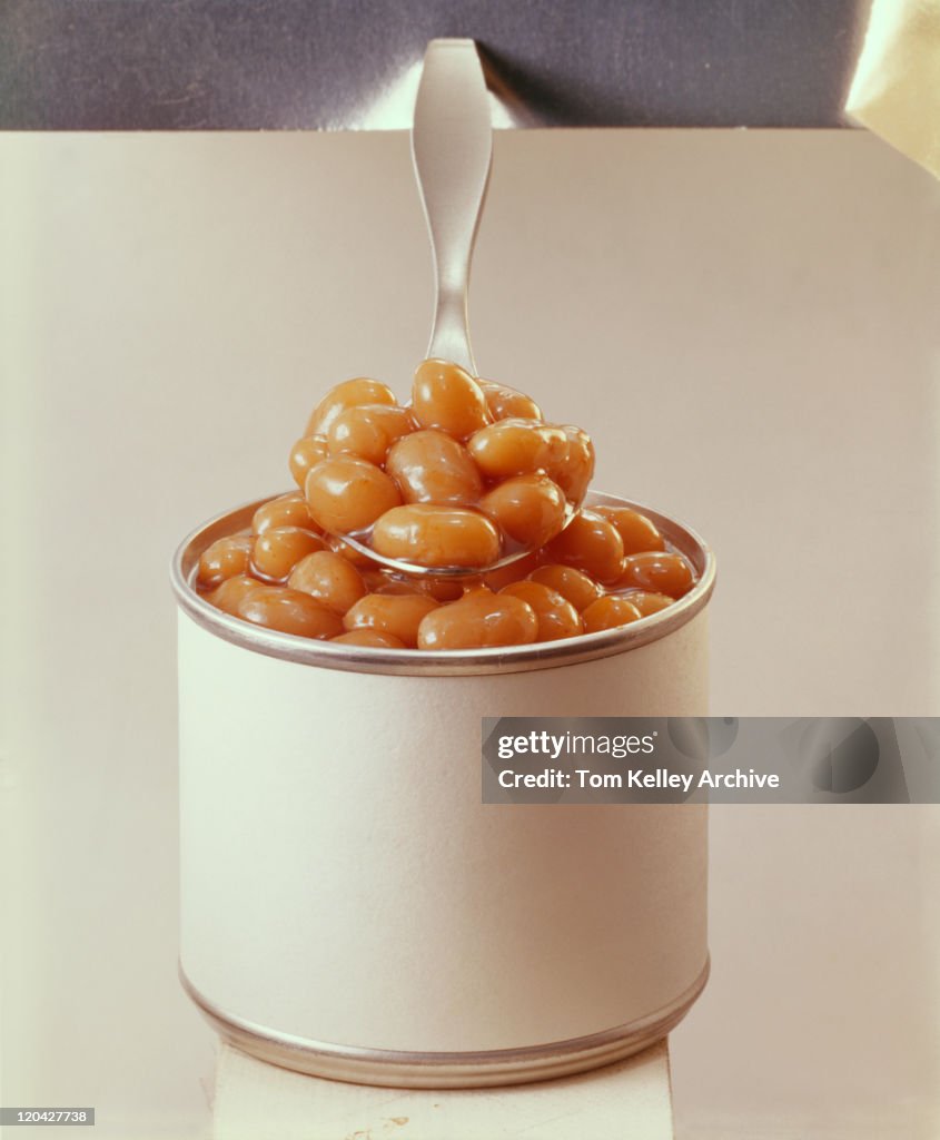 Spoonful of baked beans with tin can, close-up