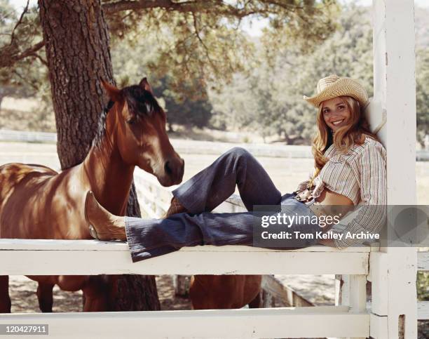 young cowgirl sitting on fence with horses, smiling, portrait - cowgirl stock pictures, royalty-free photos & images