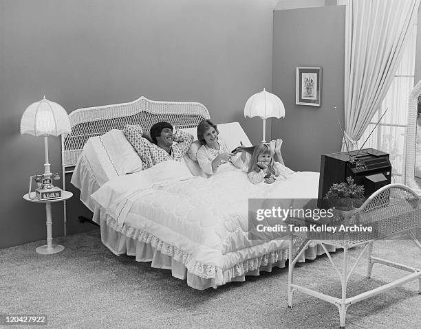 father and mother with daughter lying on bed watching tv, smiling - 1970s television set stock pictures, royalty-free photos & images