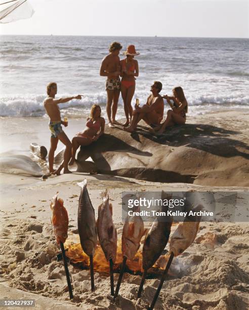 paare am strand mit fisch am offenen feuer in den vordergrund - 1975 stock-fotos und bilder