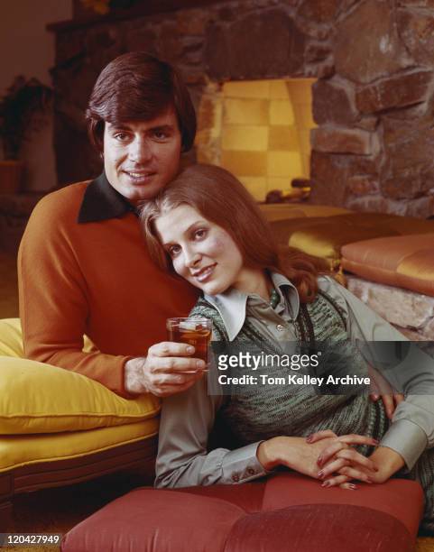 junges paar schiefen auf kissen mit drink in der nähe von kamin und smili - 1975 stock-fotos und bilder