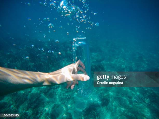 underwater shot of the hand of young woman holding clear plastic bottle with multiply bubbles outside - bottle water sport stock pictures, royalty-free photos & images