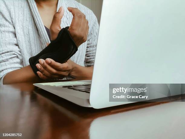 woman using laptop and wearing brace holds wrist - carpaletunnelsyndroom stockfoto's en -beelden