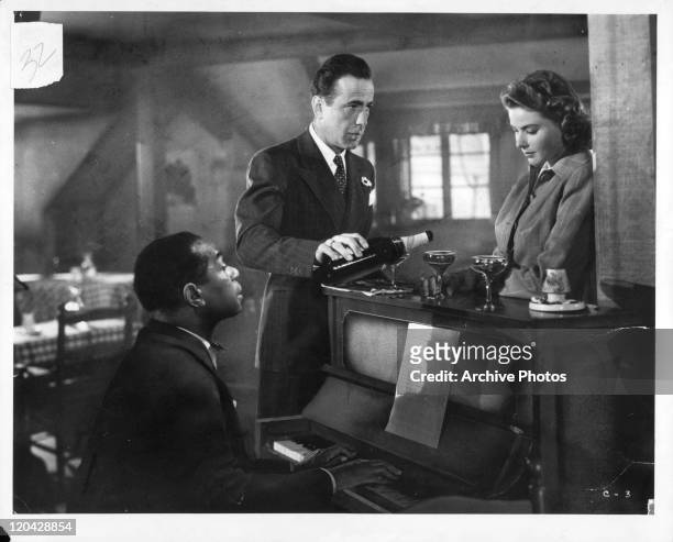 Dooley Wilson sits at the piano while Humphrey Bogart pours Ingrid Bergman a drink in a scene from the film 'Casablanca', 1942.