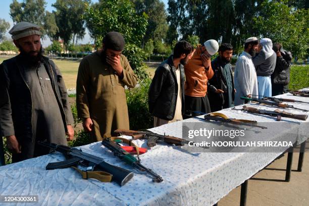 Former Afghan Taliban fighters stand next to weapons before handing them over as part of a government peace and reconciliation process at a ceremony...