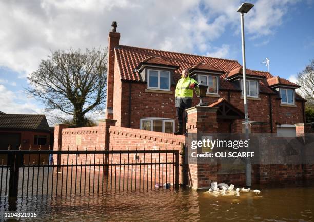 Man stands on a wall above flood water covering the entrance to a gated group of houses in East Cowick, northern England on March 1, 2020 after Storm...