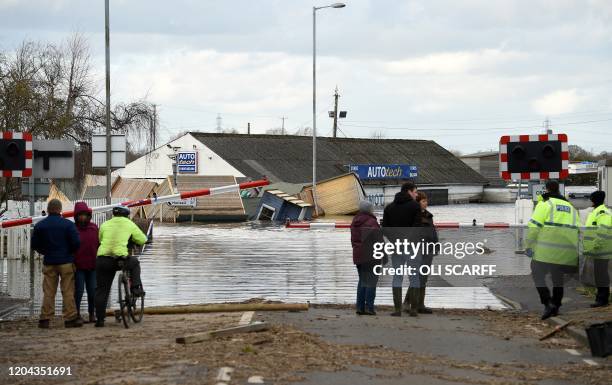 Silt covers a road as people stnad by a flooded railway train crossing in Snaith, northern England on March 1, 2020 after Storm Jorge brought more...