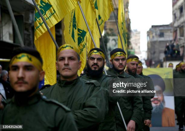 March 2020, Lebanon, Beirut: Pro-Iranian Hezbollah militants hold flags during the funeral procession of five of their colleagues who were killed in...