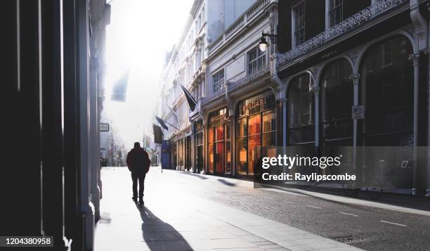 silhouetted man walking into the early morning sunshine, walking down new bond street in mayfair in central london with the high end retailer bulgari shop front warm glow standing out against the heavy morning shadows - mayfair london stock pictures, royalty-free photos & images