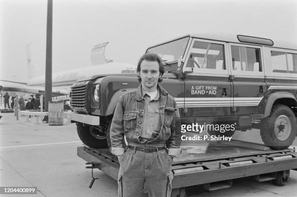 British singer-songwriter Midge Ure poses, hands in pockets, with a Land Rover Defender - 'A Gift From Band-Aid' written on the door - as the first...