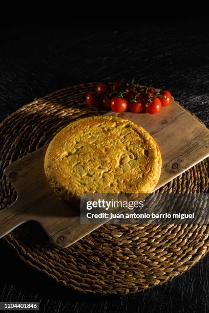 spanish potato omelette in imitation wood dishes on a rustic wicker tablecloth. cherry tomatoes. - tortilla de patata fotografías e imágenes de stock