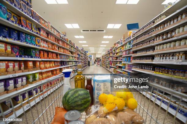 loaded shopping trolley/cart moving through supermarket aisle. - overloaded shopping cart stock pictures, royalty-free photos & images