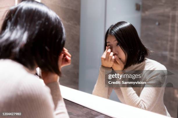 asian woman putting contact lens in eye at home - contacts stock-fotos und bilder