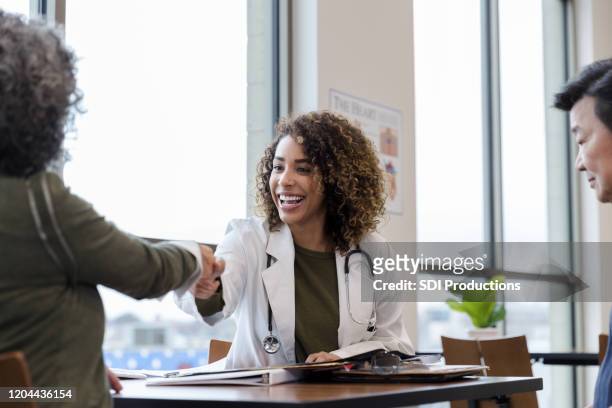 cheerful doctor greets female patient - couple shaking hands with doctor stock pictures, royalty-free photos & images