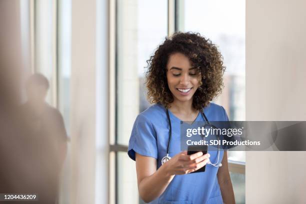 enfermeira alegre verifica mensagens no smartphone enquanto no corredor do hospital - nurse - fotografias e filmes do acervo