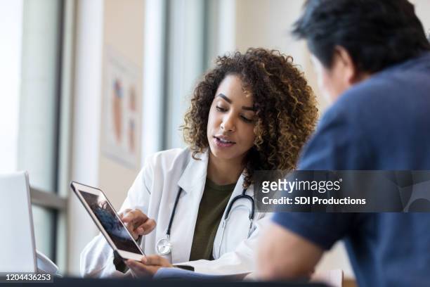 de vrouwelijke arts gebruikt tablet om x-ray aan hogere mens te tonen - gezondheidszorg en medicijnen stockfoto's en -beelden