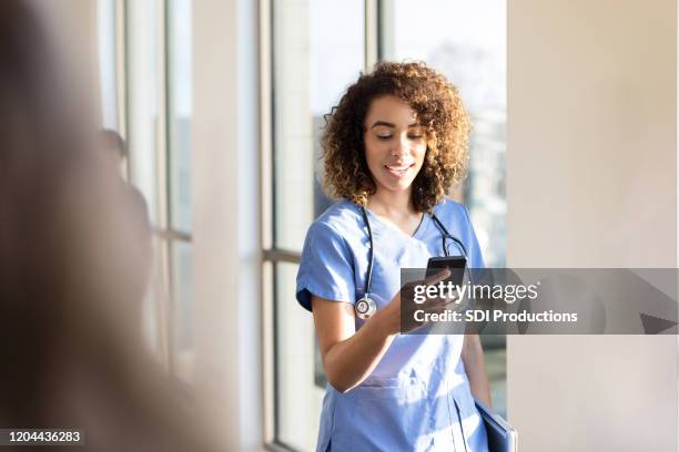 female doctor text messages as she walks down corridor - doctor looking down stock pictures, royalty-free photos & images