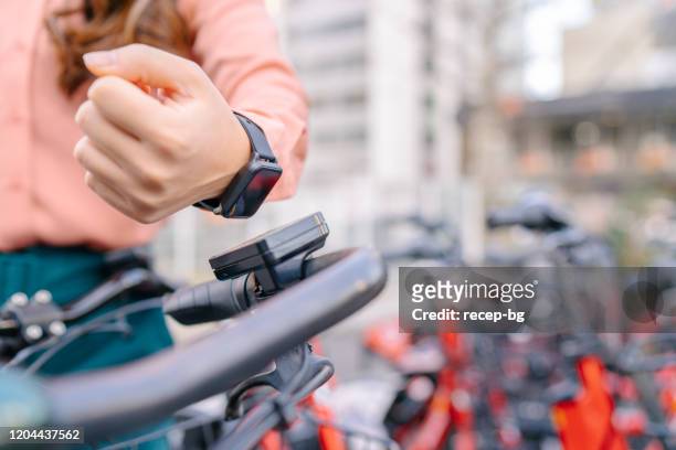 jonge onderneemster die slim horloge gebruikt om het delen fiets te huren - bicycle rental stockfoto's en -beelden