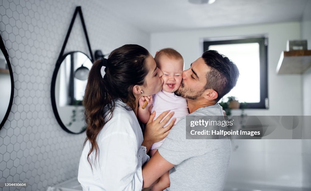 Portrait of young couple with toddler girl in the morning indoors in bathroom at home, kissing.
