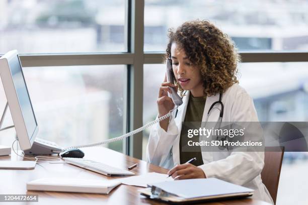 médico femenino de mediana edad hace una llamada telefónica con respecto a los registros de los pacientes - teléfono con cable fotografías e imágenes de stock