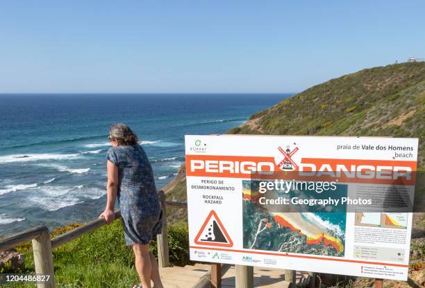 Woman looking to sea by danger notice, Praia de Vale do Homens beach, Rogil, Algarve, Portugal.