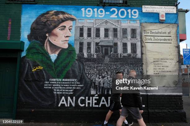 Men walk past a mural depicting The Decloration of Irish Independence alongside Countess Markievics on the Beechmount Avenue off the Falls Road on...