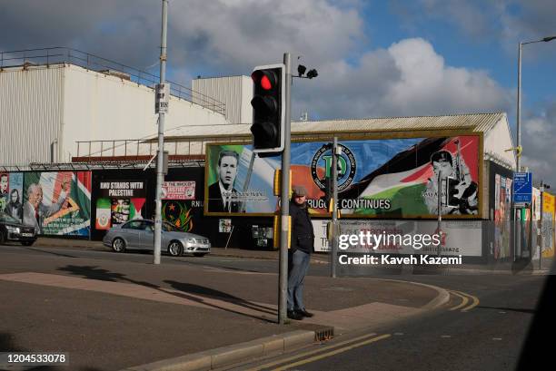 Man stands by the traffic light in front of revolutionary murals on the Falls Road on October 29, 2019 in Belfast, United Kingdom.