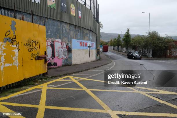 Tourist black cabbie drives near the entrance of the peace line with a mural showing a Cross with written words promising a "u201cNEW LIFE"u201d...