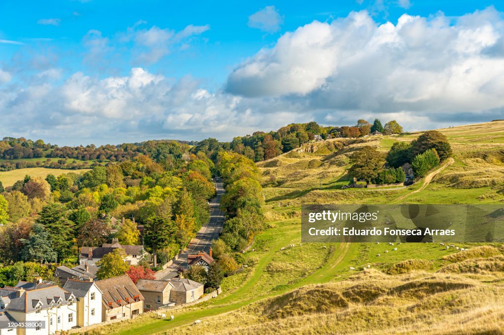 View of Cleeve Hill village, flock of sheep and rolling hills, against a sunny blue sky with clouds