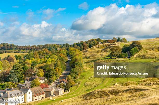 view of cleeve hill village, flock of sheep and rolling hills, against a sunny blue sky with clouds - cotswolds stock pictures, royalty-free photos & images