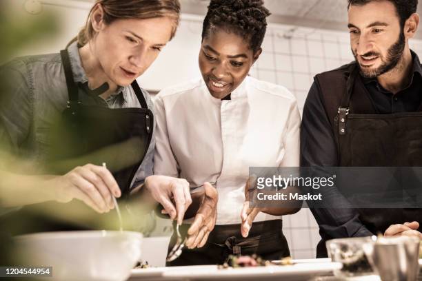 female chef teaching students serving food in plate in cooking class - apron stockfoto's en -beelden