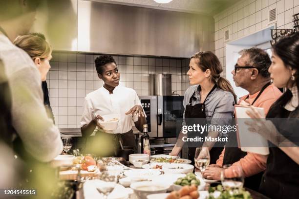 female chef giving instructions to adult students standing around table in cooking class - cours de cuisine photos et images de collection