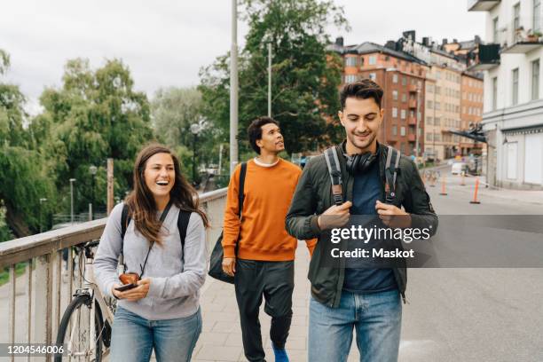 smiling friends walking on street while exploring city during vacation - group of friends walking along street fotografías e imágenes de stock