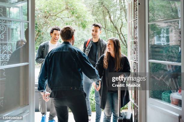 rear view of owner handshaking with guests while standing in doorway - location immobilière photos et images de collection