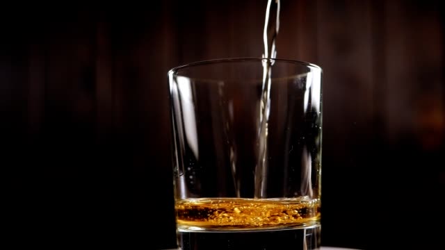 Close-up of whiskey poured into a rotating glass on a black background.