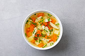 Chicken soup with vegetables in white bowl. Grey stone background. Top view.