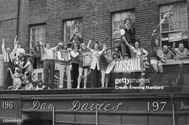 Supporters of Arsenal FC wave and cheer on a balcony in Upper Street as they greet the team riding in an open top bus on a victory parade through the...